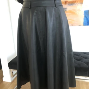 Läder kjol - Immitationsläder, mjuk och lätt material Blixtlås i sidan Midja mått 68 cm Längd 66 cm Använd några få gånger