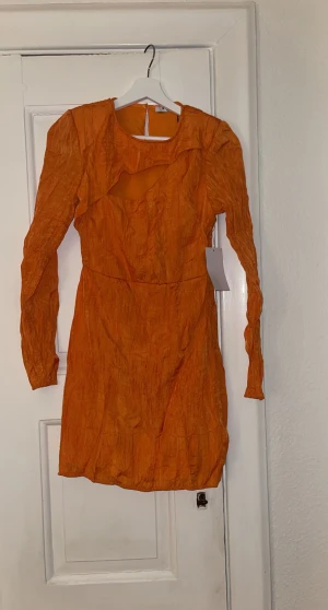 Klänning - Orange miniklänning. Sitter inte för tight, outcut ovanför brösten. Miniresår längst ner och i ärmarna som på bild. Lappar kvar - aldrig använd 
