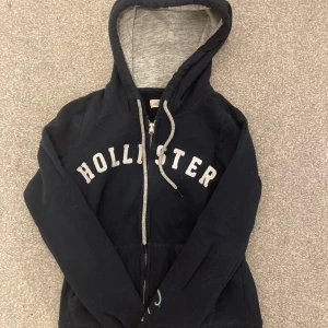 Hollister hoodie - En hollister mörkblå zip upp hoodie med vita bokstäver. Har själv använt hoodien 2-3 gånger men köpt köpt secondhand. Används tyvärr inte då den är förlusten för mig:( Om du har funderingar eller frågor skriv gärna!!!!!