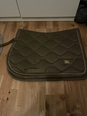 Equestrian Stockholm schabrak  - Jättefint schabrak i färgen champagne från Equestrian Stockholm, schabraket är i storlek full och är använt max 10ggr. Schabraket köpte jag nytt och är väldigt sparsamt använt. Det har en jätteliten rostfläck på märket (se bild) annars nästintill nytt 450