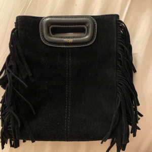 Maje väska! - Säljer min jättefina Maje väska , den lilla storleken. Kvitto,dustbag och påse medföljer. Är väl använd men syns inte mycket då den är svart och mocka (lite smutsig) Frakta/mötas upp på Östermalm. Den guldiga kedjan är lite rostig men den svarta är oanvän