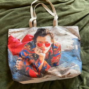 Harry styles strandväska - Denna Harry styles strandväska är i perfekt skick! aldrig använd! det är officiell merch. denna köptes för ca 650kr. Jag säljer den nu för 550kr +frakt. det är samma tryck på båda sidorna. Inga innefack. hör av dig vid intresse ❣️❣️