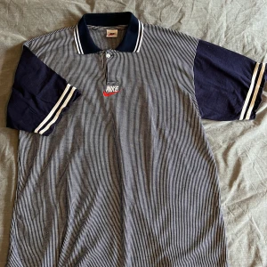 Nike Piké  - Blå/vit randig Nike piké. Det står ingen storlek men känns som L/XL.  Längd: 70cm Bredd över bröst: 61cm Bredd midja: 61cm 