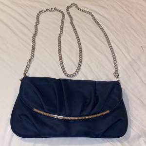 Marinblå kuvertväska som är använd en gång. Välan har en avtagbar silver kedja. På framsidan är det en en detalj av diamanter.