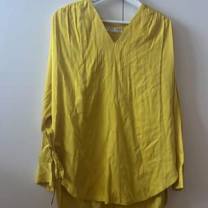 En gul Skjorta/klänning som har två söta band som kan knytas. Oanvänd och i bra skick. 