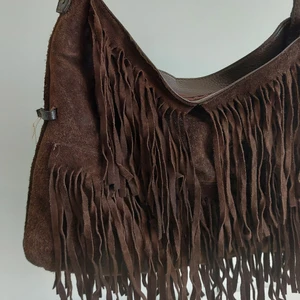Väska med fransar  - Brun axelremsväska med fransar på fram- och baksidan. Detaljer i guld och ett fack på insidan. Priset är exklusive fraktavgift. 