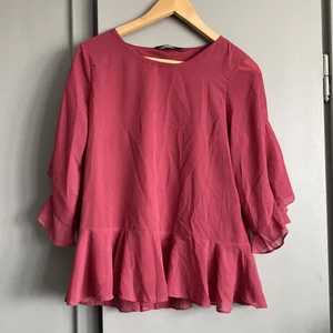 Blus  - Plommonlila blus med volang längst ner och vid ärmarna. Stl M