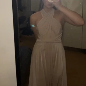 Balklänning - Maxiklänning som går att knyta på olika sätt och är öppen i ryggen. Den är latte/ ljusrosa i färgen. Helt oanvänd eftersom den aldrig kom till användning. Köpt för 1099kr