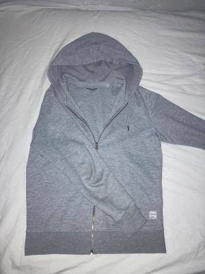 Grå Zip Hoodie - Grå zip hoodie från Jack & Jones. Köpt på Zalando. Ganska tight modell. Nästan för liten på mig (jag är 182 cm)