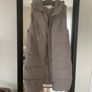 Beige vadderad väst strl S  - Beige vadderad väst från H&M. Längre modell med luva. Otroligt snygg och skön. Inköpt i vintras och använd några enstaka gånger.  
