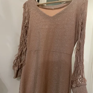 Glittrig klänning  - En jätte fin glittrig klänning med färgen bronze. Använd en gång och den är jätte fin och har en detalj vid armarna som gör att klänningen ser speciell ut.Man kan även ha en bälte på midjan som ger en extra detalj är ni intresserade skriv till mig ❤️ 