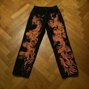 Svart och orange jeans  - Svarta jeans med orange mönster på framsidan  Köparen står för eventuell frakt 