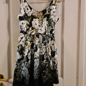 Klänning HM 34 - Blommig klänning i glansigt tjockt tyg från HM i storlek 34. Ny med lapp kvar. Stängs med dragkedja längs ena sidan under armen. Innertyg i hela klänningen  Aldrig använd.  Frakt tillkommer med 59 kr 🌞