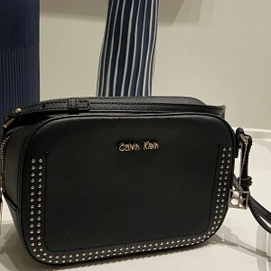 Calvin Klein väska - Jättefin väska från Calvin Klein. Jättefint skick men lite missfärgning på hänget man stänger väskan med. B 22 x h 15 