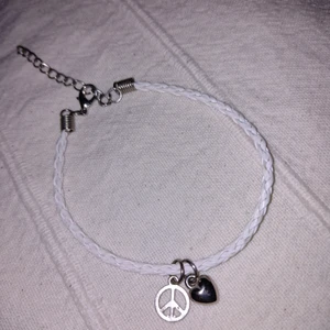 Oanvända vitt "flätat" armband - peace & love  - Oanvända vitt flätat armband med silverfärgade berlocker (hjärta och peacemärke) och lås. Storleken går att justera. Frakt 15 kr.