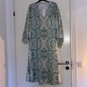 Vit/grön mönstrad klänning - Vit/grön mönstrad långklänning med långa puffiga ärmar! Storlek s/m. Super fin till sommaren med bikini under eller med skärp i midjan! Köpt för 699 från Kenja i Malmö! Aldrig använd med lappar kvar, Säljer eftersom den inte passade men retur var ej möjlig! Frakt ingår i priset!