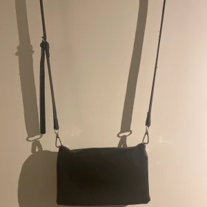 Väska - Svart väska med justerbart band, som kan plockas av. Har tre fack. Är lite sönder på insidan av 1 tack, inget som syns när väskan är stängd. Hör av er för mer info 🥰