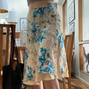 Blommig kjol i fint skick med slits längst ned. Beiget undertyg. Blåa och rosa blommor. Kjolen går ungefär till knäna. 