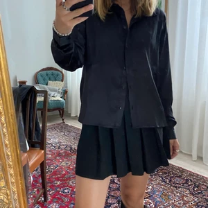 Svart glansig Skjorta stl. S - En svart glansig skjorta från JDY köpt i London. Har aldrig använt och prislappen sitter kvar. Den är true to size och i en kortare modell. 