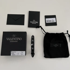Valentino armband - Säljer mitt fina valentino armband i svart färg med silvriga nitar. Väldigt  stilrent armband till våren eller sommaren som passar perfekt under solen. Helt nytt, allt medföljer, såsom extranitar, dustbag och låda. Finns även köpebevis, garanterad äkthet.