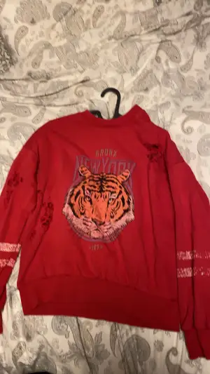 En röd tröja med tryck av en tiger. Kommer från ginatricot och är en fin höst/vår tröja till alla typer, passar även folk med storlek medium 