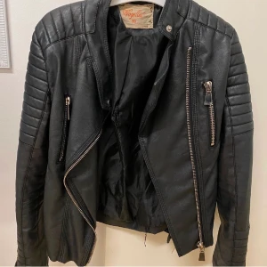 Skinnjacka  - Mc-inspirerad jacka i läderimitation med quiltade detaljer på axlar och i ärmslut. Två fickor med dragkedja framtill. Nästan som ny! Passar både 36/38