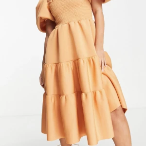 Ljusorange midiklänning - Ljusorange midi klänning, med smockning och puffärmar  Storlek: 32 Märke: ASOS Använd 1 gång, nyskick   Köpt för 849kr