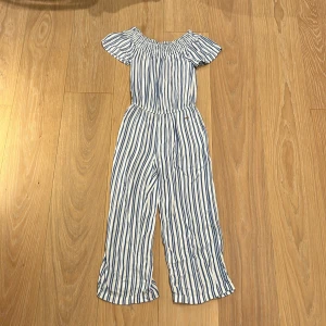 Byxdress  - En vit och blå byxdress i storlek 134 som kommer ifrån Kappahl. Använd mycket men i ett bra skick. Långa ben och kort i armarna med volang upp till och har resor band så den är väldigt töjbar.  Har två fickor fram till och i mitten har den också resor. 