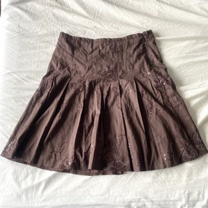 Brun kjol  - Brun kjol med blommiga mönster och paljetter. sitter lågmidjat på mig som har XS. Om man ej vill ha lågmidjat passar den S-M. Kjolen är i  bra skick, inga hål eller fläckar. finns en dragkedja på sidan av kjolen, den funkar perfekt. Köpare står för frakt