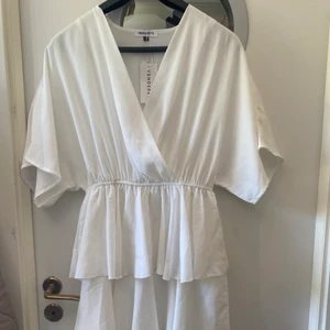Oanvänd klänning - Oanvänd klänning från danska märket Venderbys. Köpt till studenten men valde att ha en annan. Vit, volang och omlott topp. Visa ärmar. 