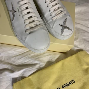 Axel Arigato skor, ”clean 90 bird” storlek 39 - Jättefina vita/silvriga sneakers ifrån Axel Arigato! Skorna är i bra skick och använda endast max 10 gånger då passformen är lite för smal på min fot. Skorna kommer i sin original kartong med en tillhörande dustbag (se på bilden) Köparen står för frakten!