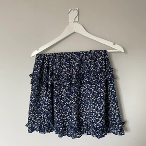 Mörkblå kjol med vita blommor  - Somrig blå kjol med vita blommor och volang. Storlek M men passar L också då det är bra resår i midjan. Säljer pga dålig användning 💙 Köparen står för frakt! 