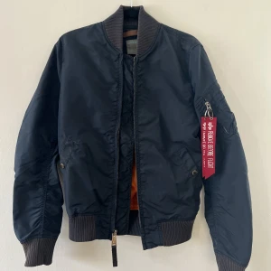 Alpha Industries bomberjacka - Säljer min blå alpha industries bomberjacka då den inte längre kommer till användning. Den är i använt skick men utan större skavanker. Krage och ärmmuddarna är lite solblekta annars är jackan i bra skick. Nypris 1300:-