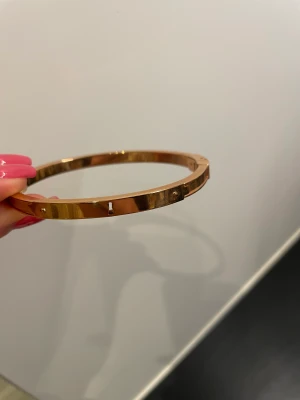 Armband nyckel - Stelt armband med detaljer i form av nyckelhål och nyckel. Öppnas genom knäpp-mekanism (bild 2, nyckel) . Roséfärg