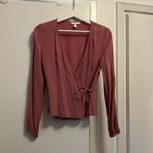 Jacuardvävd omlottblus, rosa, H&M stl.36 - Gammelrosa V-ringad omlottblus. Två knytningar och en hyska för stängning av blusen. Tunn söm för att markera midjan och självfall i tyget under sömmen. 