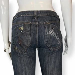 Lågmidjad Skinny Jeans - Lågmidjade skinny y2k jeans i fint skick. Några kristaller som saknas både fram och bak. Några andra få tecken på användning finns. Okänt märke och material. Lite tajt för dockan.Mått: Höftbredd 36cm, Grenlängd 17cm och innerbenslängd 80cm.