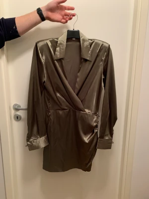 Grön klänning - Oanvänd, stor i bysten Bilden gör ej färgen rättvis, starkare olivgrön i verkligheten! Kan skicka andra bilder på färgen vid intresse. Glansigt material. Går till ungefär mitten på låren.