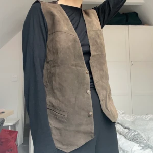 Brun väst i mocka - Brun mockaväst köpt second hand. Baksidan av västen är i ett annat glatt material som syns på bild två. Säljes pga för stor.   Kan skickas med postnord, och då tillkommer fraktkostnad! 🌷