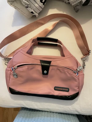 Axelväska  - En rosa handväska med många fack. Bandet går att göra längre samt kortare, mycket sparsamt använd. 28 cm bred och 18 cm hög Vinylaktigt material. Inga fläckar eller skador på.