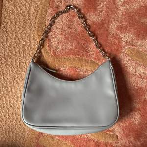Ljusblå/himmelsblå handväska i fejkläder med silverfärgad kedja. Använd 1 gång, ren och fin inuti. Mäter ca 27x15cm