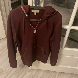 Burberry hoodie  - Vinröd burberry hoodie i storlek L. Köpt på kaspersheat. Säljer då den börjar bli liten, är i exceptionellt skick, inget att klaga på. Riktigt skön, fin hoodie. Nypris ca5000kr