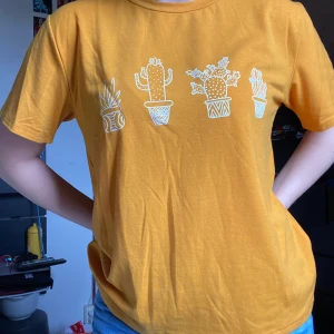 Gul T-Shirt  - En senapsgul t-shirt med vita kaktusar på. Storlek S