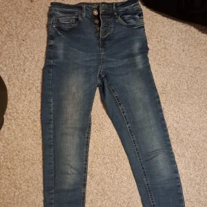 Jeans - Säljer dessa jeans från Noisy May. Det går ej att köpa mer. Säljer pga för små. Storlek w25/L30. Urprungspris är 399 kr jag säljer för 100 kr. Passar till både bred och smal midja men as snygga på timglaskroppen med croppad topp. De har knappar.