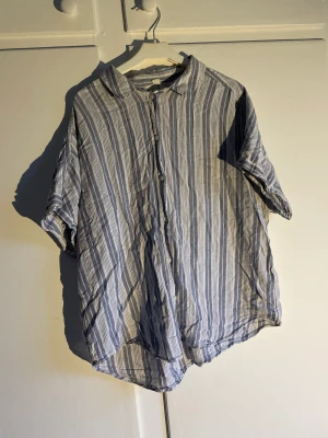 Kortärmad skjorta - Blå och vitrandig. Vita knappar. Tunt och skönt material. Kan bäras både ensam eller uppknäppt över t.ex en croptop! Hör av dig om du undrar något!
