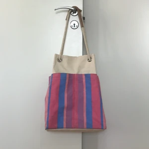 Väska - Naturvit väska med färgglada ränder på, ca. 40cm bred och 40cm hög i utplattat läge (men blir mer avlång när man har den på sig). Bra storlek för stranden!