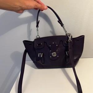 RALPH LAUREN ”rickybag”  - Handväska i kalvskinn, färgen är lila, RL rickybag i minsta modellen, den är använd sparsamt och har några få repor. Finns långt och kort band och båda är avtagbara. Nypris: 12.000 SEK. Inköpt på biblioteksgatan i Stockholm på deras flagship.