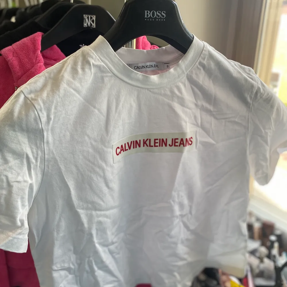 Vit croppad T-shirt från calvin Klein jeans med röd text, storlek S. Skrynklig på bilden men försvinner om man stryker/tvättar☺️. T-shirts.