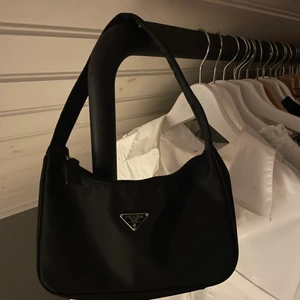Pradaväska - Snygg, stilren och populär Pradaväska. Tror inte den är äkta men är i alla fall en fin kopia. Tidlöst snygg oavsett! Mycket bra kvalitet, känns rejäl. Skickar gärna fler bilder om så önskas. Köpte secondhand för 700 kr.
