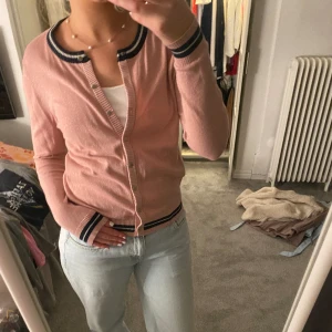 Neo noir kofta - Storlek L men sitter som  M. En fin ljusrosa glittrig kofta med marinblå/vita detaljer. Guldiga knappar o fint skick. 