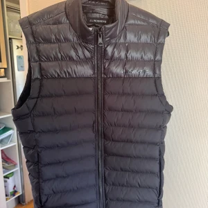 J Lindeberg Väst  - J Lindeberg väst svart. Storlek M men sitter som en S  Köpt i Lindeberg butiken i STHLM  Endast använd ett fåtal gånger då den nästan var för liten när ja köpte den.  Enda defekten är två små små hål, se de sista bilderna.